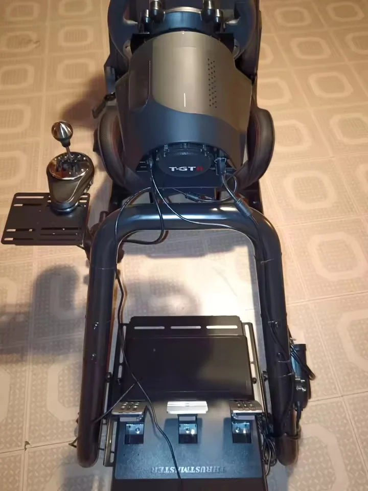 Pohľad zhora na kokpit s volantom Thrustmaster T-GT II, radiacou pákou a pedálmi.